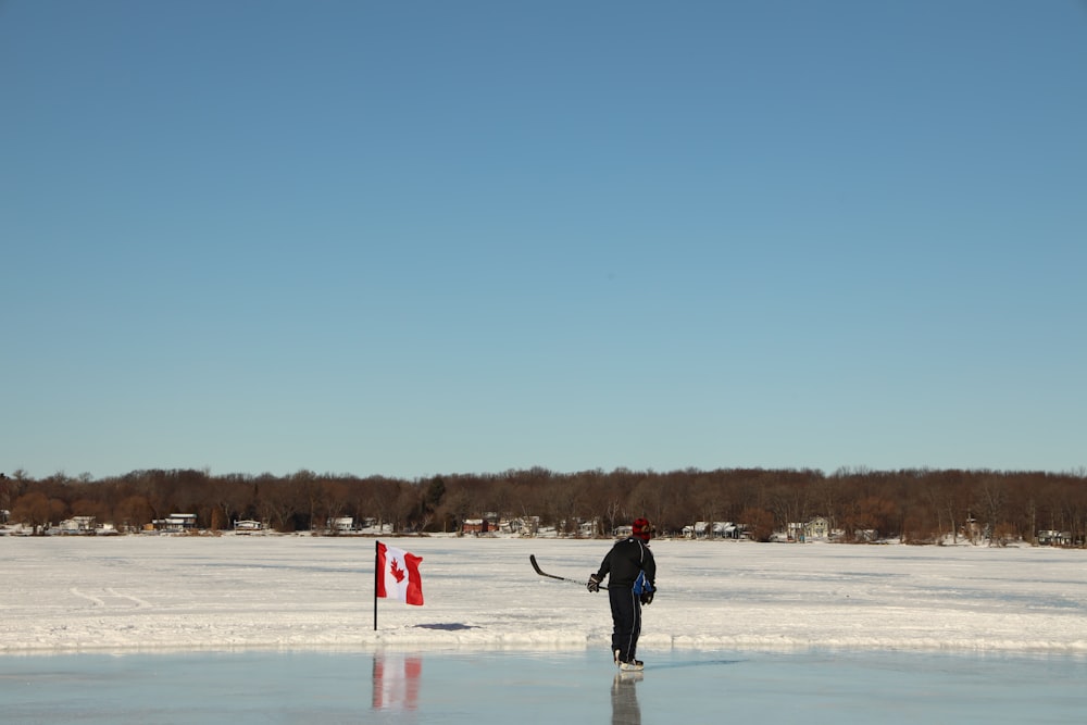 man in black jacket and pants holding red and white flag on snow covered field during