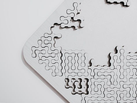 An abstract wooden puzzle piece with intricate and interconnected grooves and patterns, set against a plain background. The piece appears to be part of a larger modular structure.