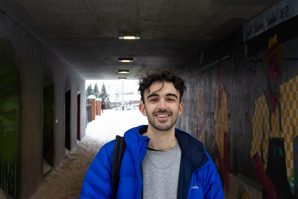 man in blue and gray hoodie standing near brown wooden wall during daytime