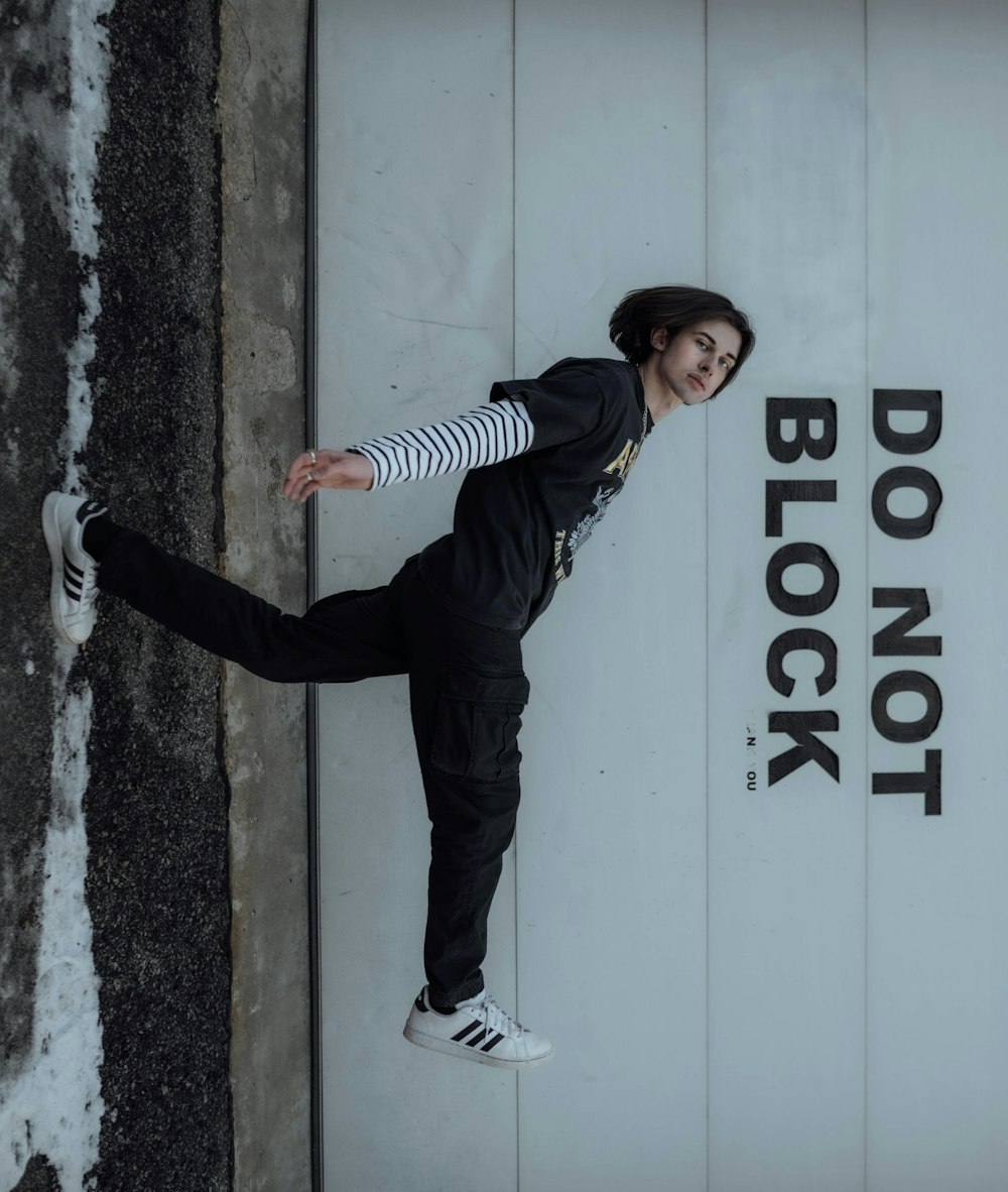 man in black and white striped long sleeve shirt and black pants leaning on white wall