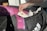 A hand holding a tube of muscle relief cream is reaching into a black sports bag. Inside the bag, there is a pink rolled-up yoga mat with floral patterns and a purple heavy resistance band. The bag also contains white items, possibly clothing.