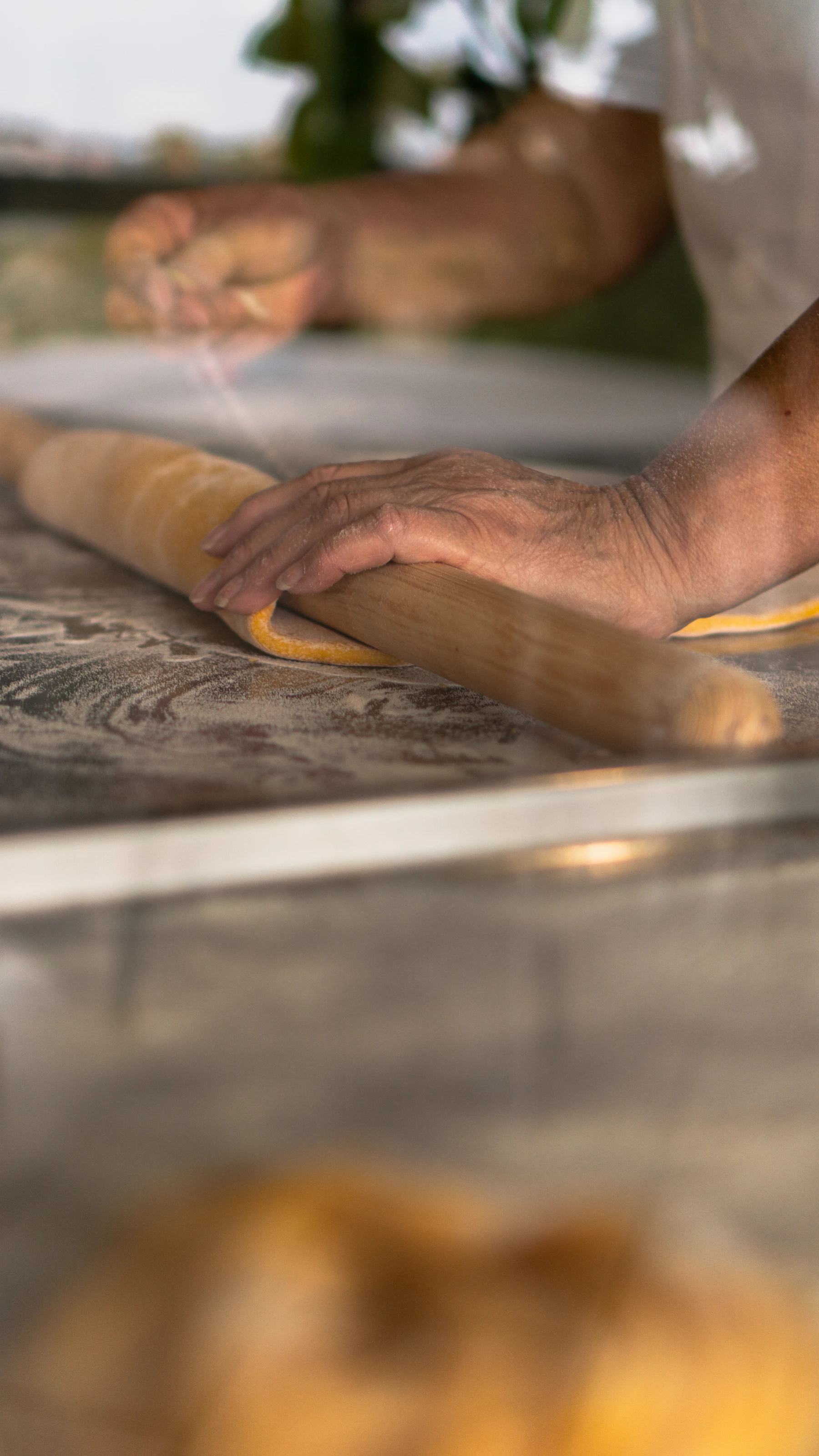 Hands rolling a sheet of egg pasta around a long wooden pin on a floured table
