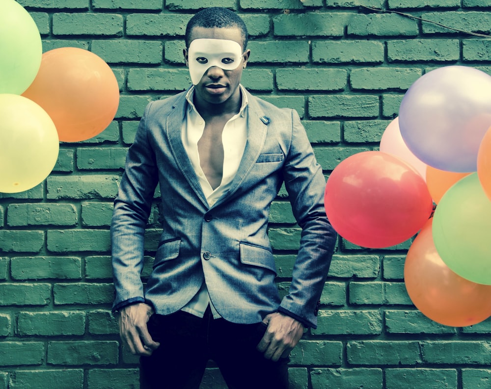 man in blue button up jacket and black pants standing beside wall with balloons