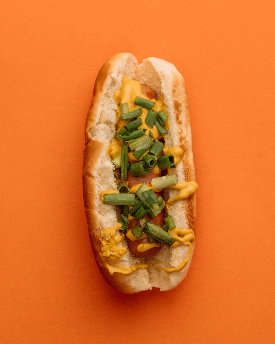Hot dog topped with cheese sauce and green chilies on a bright orange background