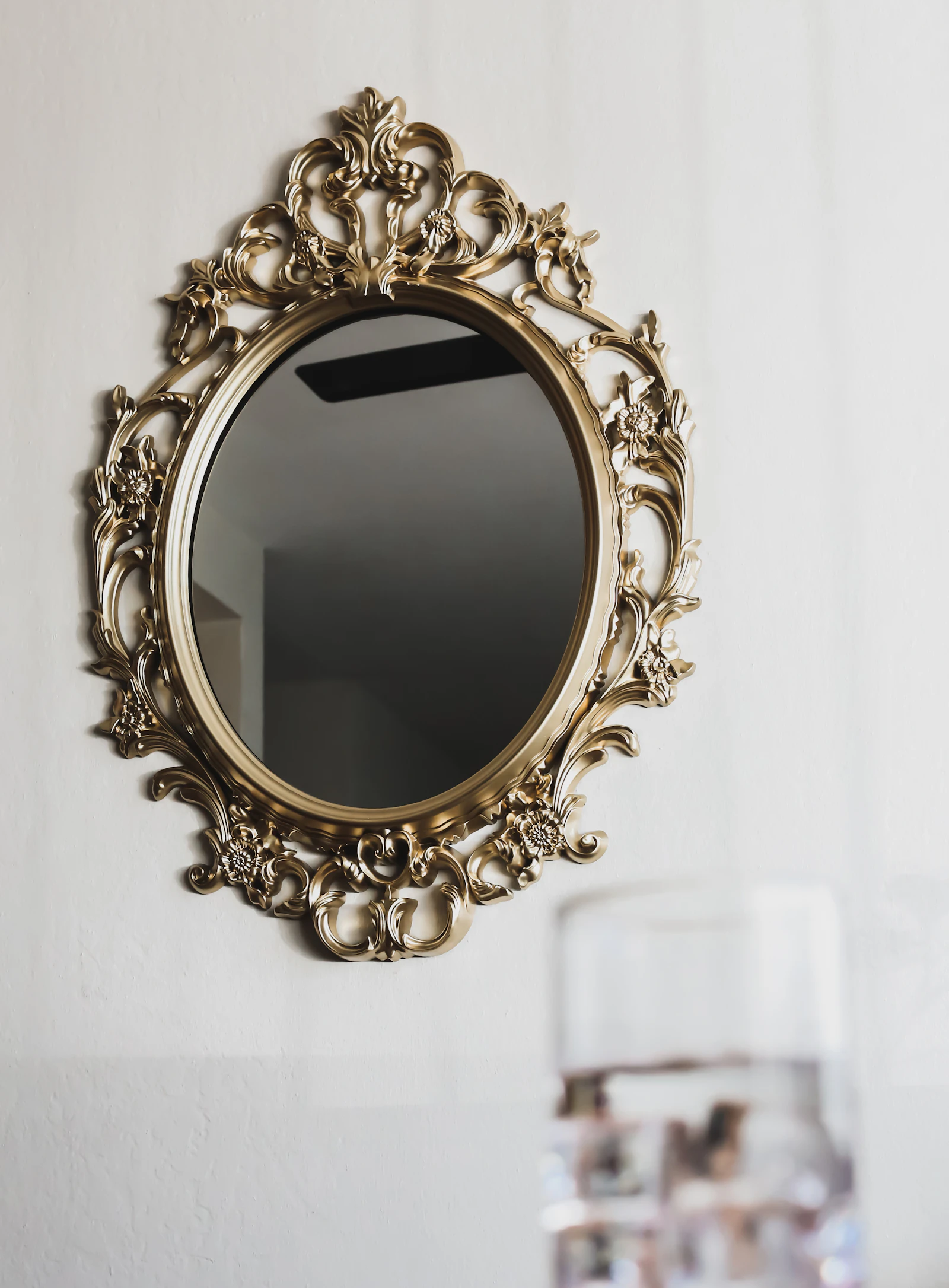 Miroir ovale au cadre doré ouvragé accroché à un mur clair