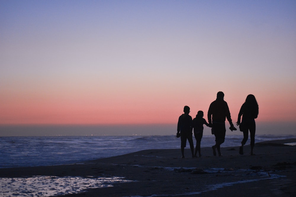 日没時にビーチに立っている 3 人の男性と女性のシルエット