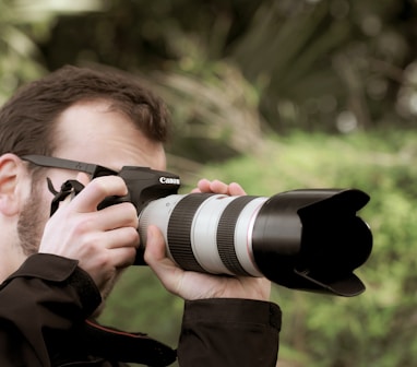 man in brown jacket holding black dslr camera