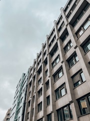 A modern office building with a geometric facade featuring numerous windows. The structure appears tall and is set against a cloudy sky, giving an urban and professional feel.