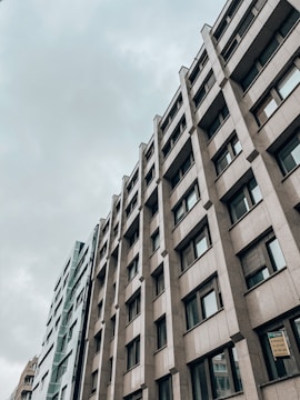 A modern office building with a geometric facade featuring numerous windows. The structure appears tall and is set against a cloudy sky, giving an urban and professional feel.