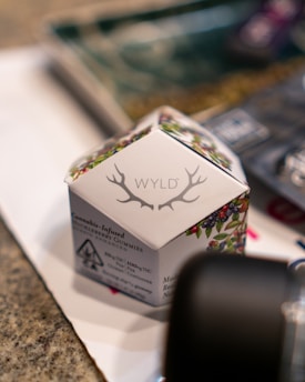 A box labeled 'WYLD' with antler-like designs contains cannabis-infused huckleberry gummies. The packaging includes natural imagery such as berries and leaves, emphasizing organic ingredients. The box displays a THC content label and a cannabis symbol, indicating the product's characteristics.