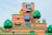A colorful and vibrant landscape from a video game world featuring cartoon-like hills, animated trees, recognizable characters, and interactive elements such as blocks and clouds. The scene is layered with textures that resemble stone and grass, and includes elements like a large, menacing stone face and a stack of small creatures.