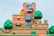 A colorful and vibrant landscape from a video game world featuring cartoon-like hills, animated trees, recognizable characters, and interactive elements such as blocks and clouds. The scene is layered with textures that resemble stone and grass, and includes elements like a large, menacing stone face and a stack of small creatures.