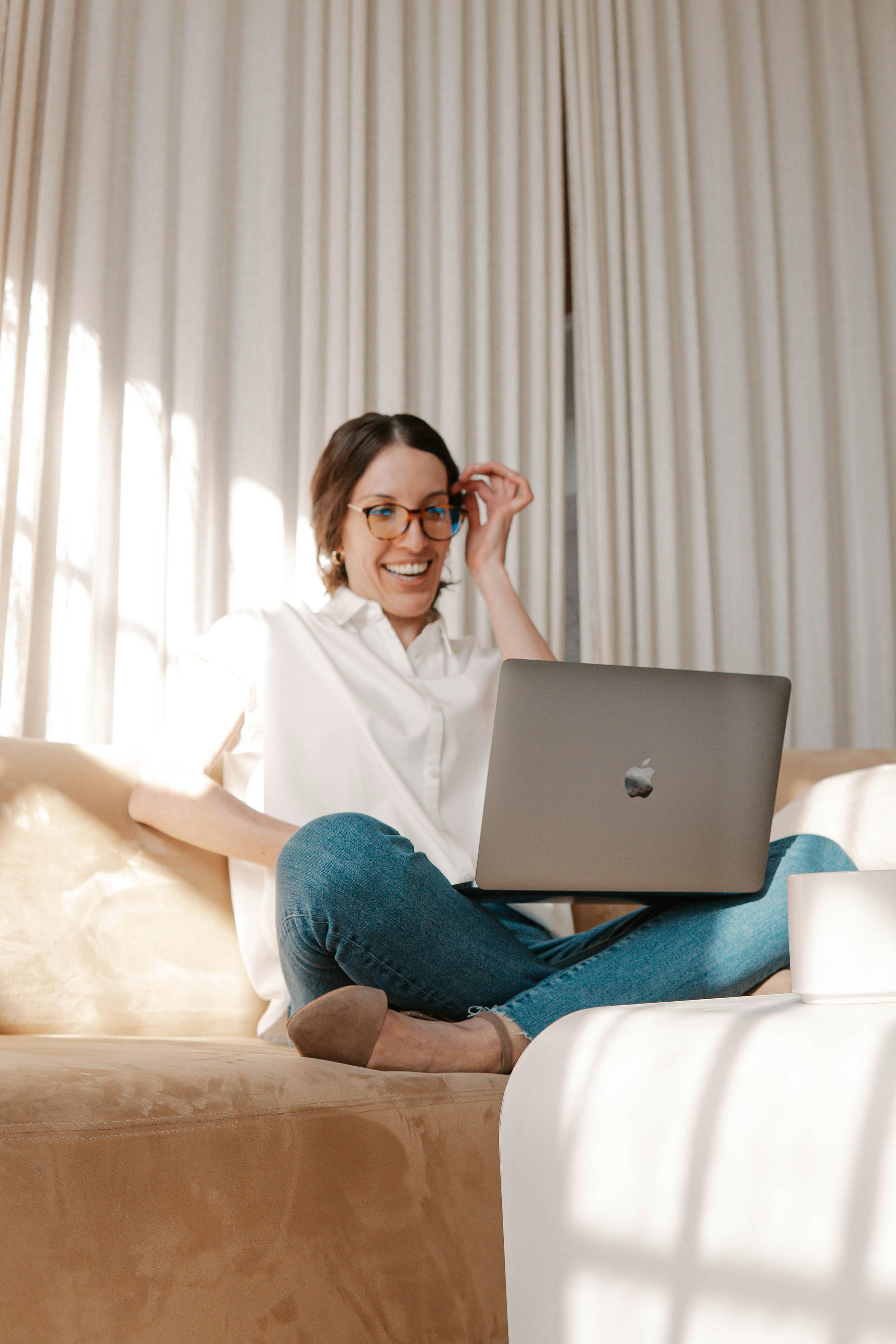 woman in white button up shirt and blue denim jeans sitting on bed using macbook