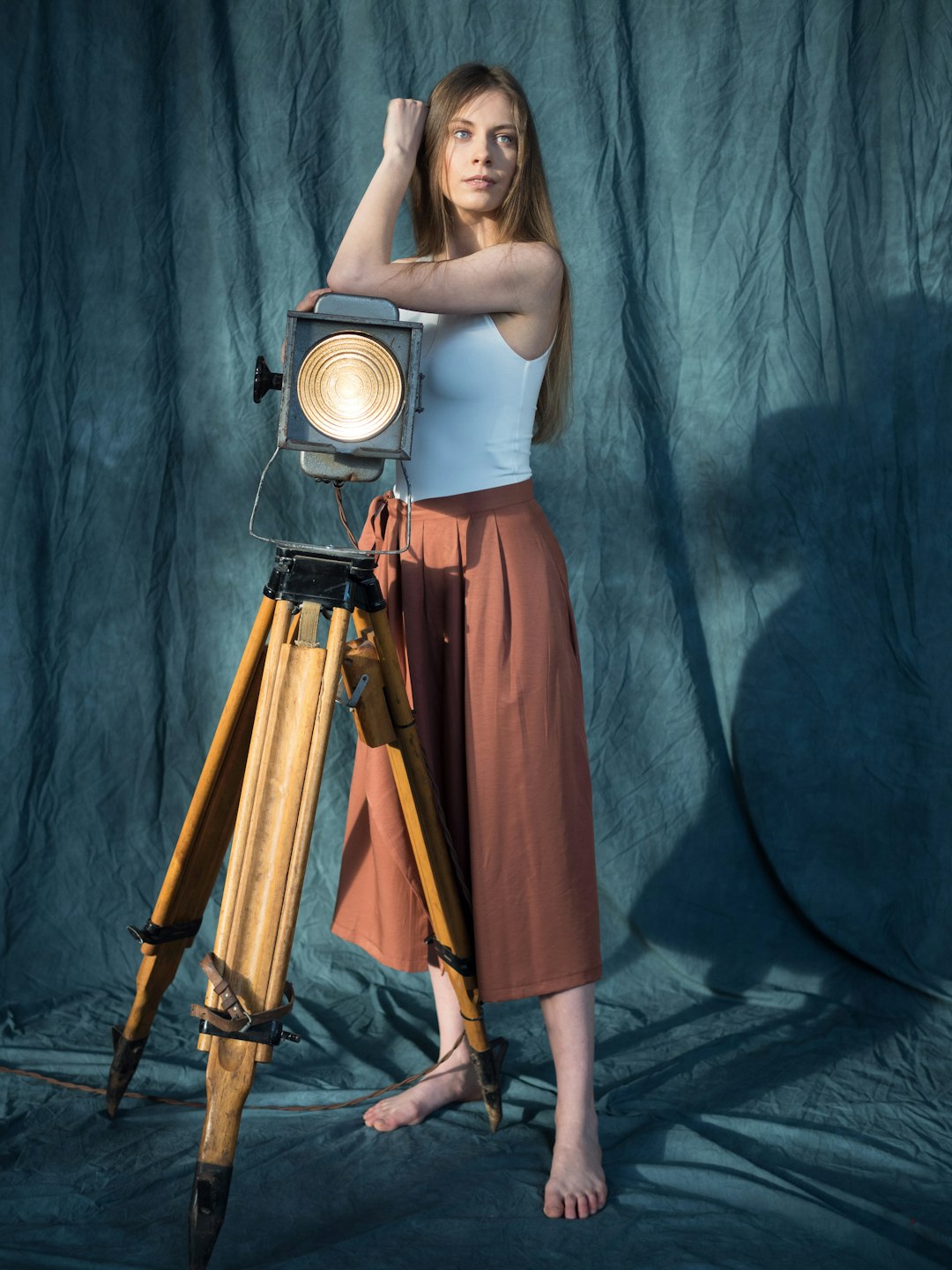 woman in white tank top and orange skirt standing beside black and brown tripod