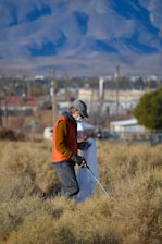 man in orange jacket and black pants with black backpack walking on green grass field during