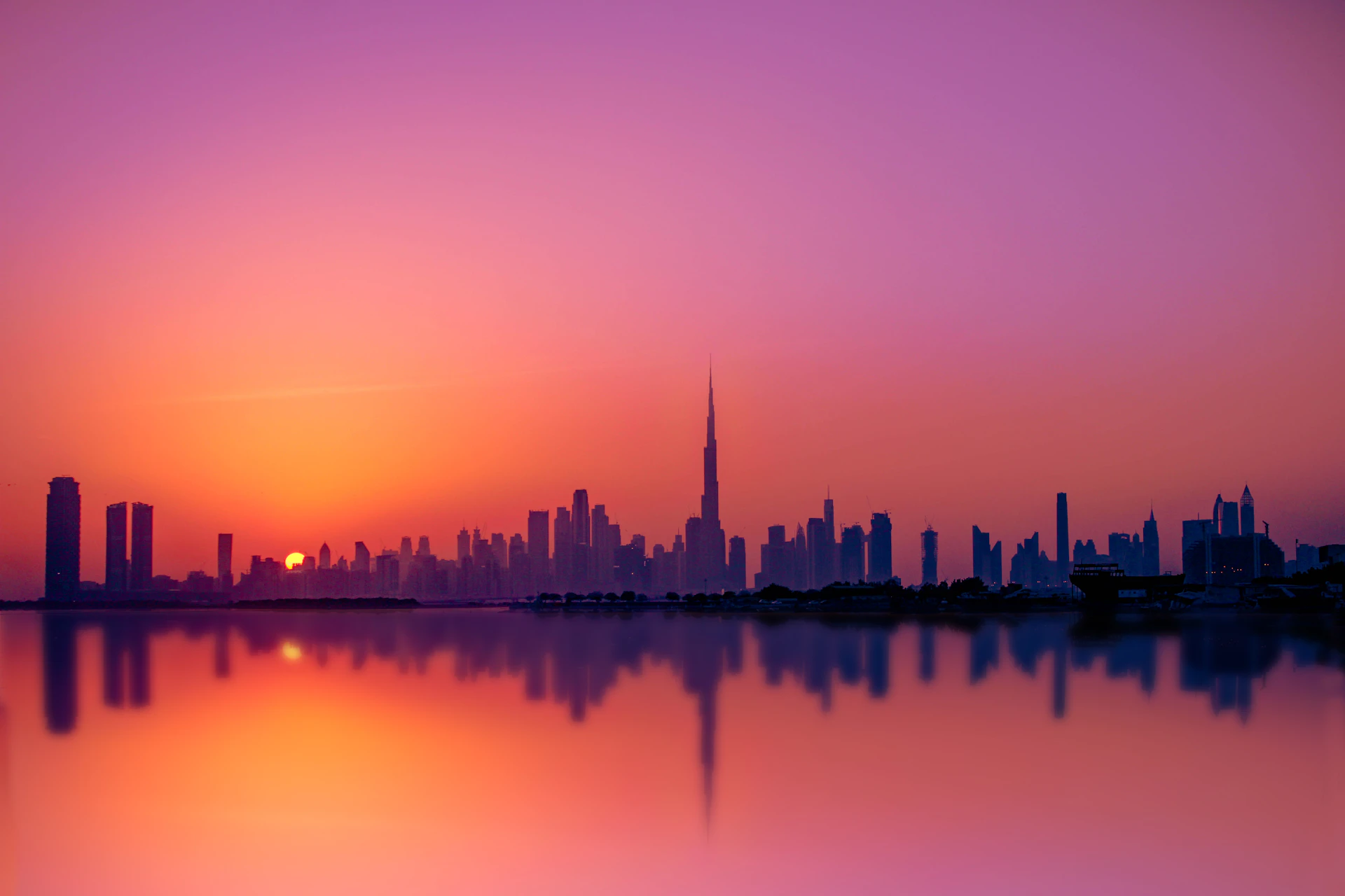 Dubai's skyline silhouetted against a pink and gold sunset, with the Burj Khalifa at its center