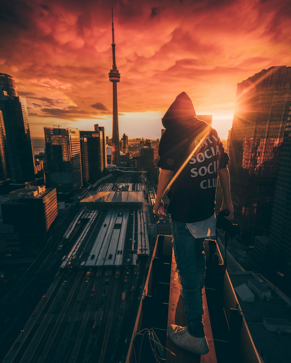 man in black and white hoodie standing on the roof of a building during sunset