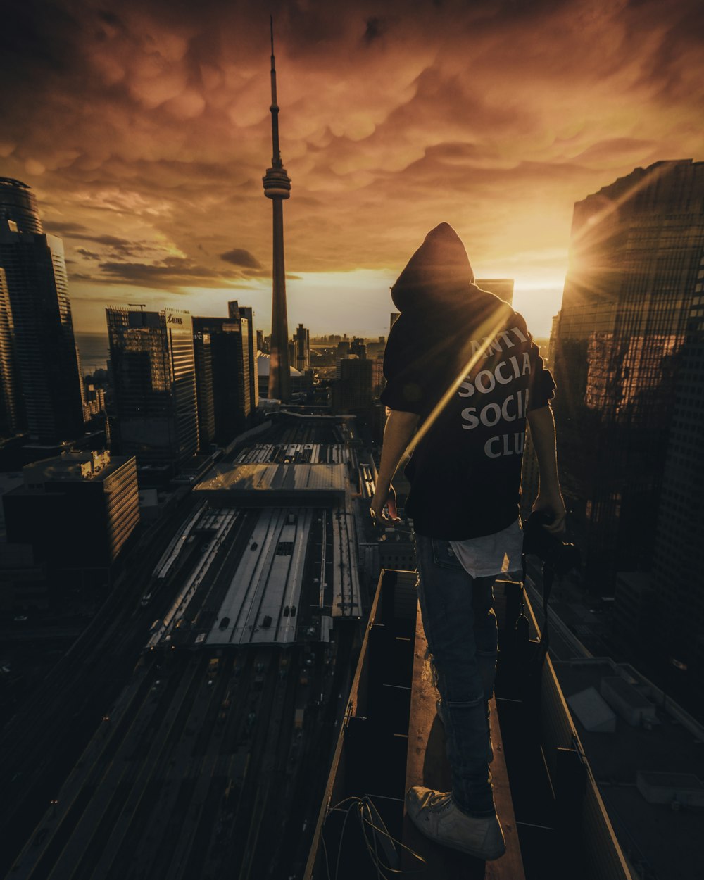 man in black and white hoodie standing on the roof of a building during sunset