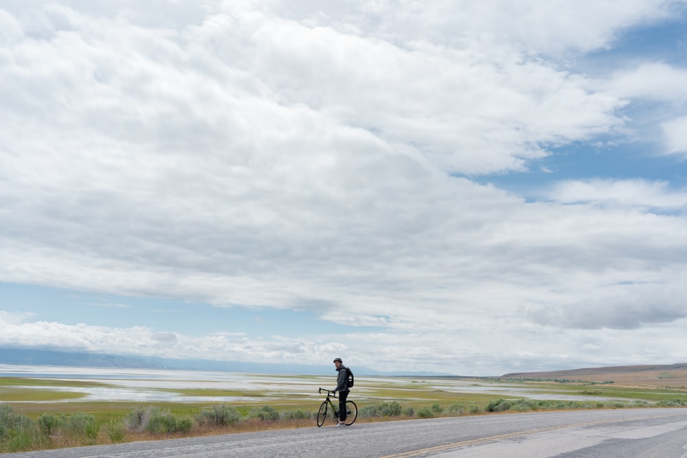 Mann in schwarzem Hemd und schwarzer Hose beim Fahrradfahren auf grauer Asphaltstraße unter weißen Wolken