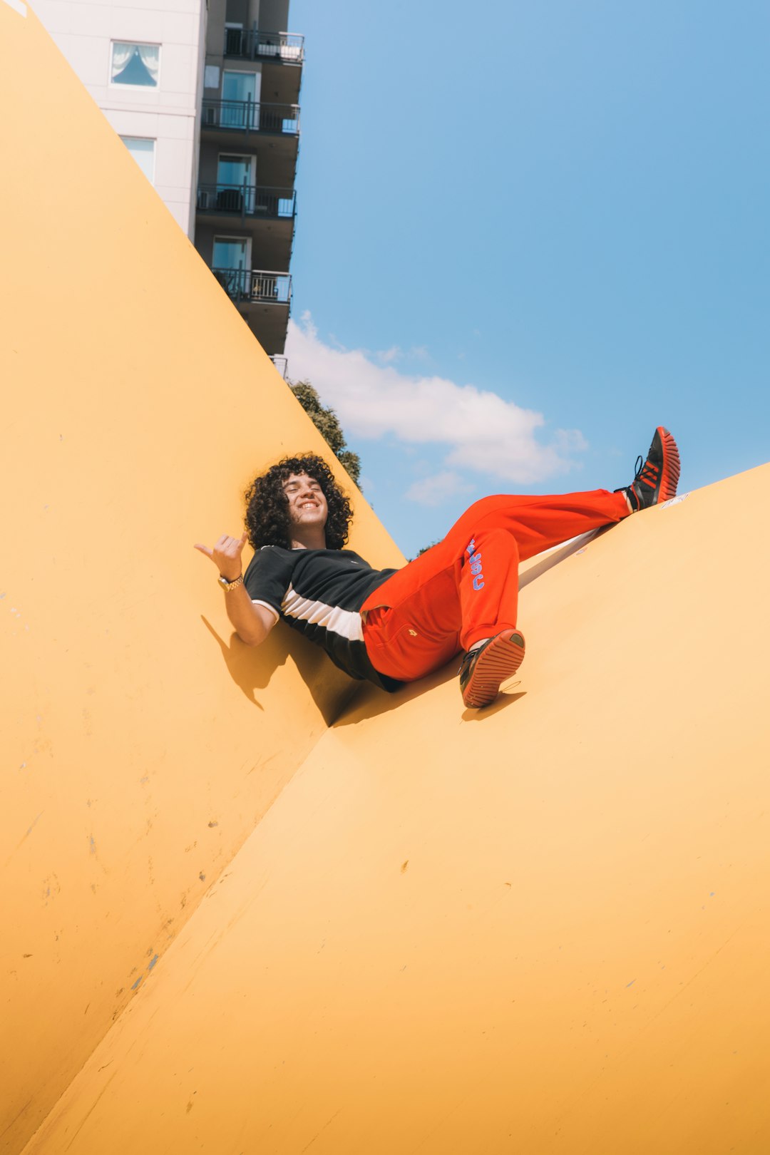 woman in red and black long sleeve shirt and black shorts lying on yellow concrete wall