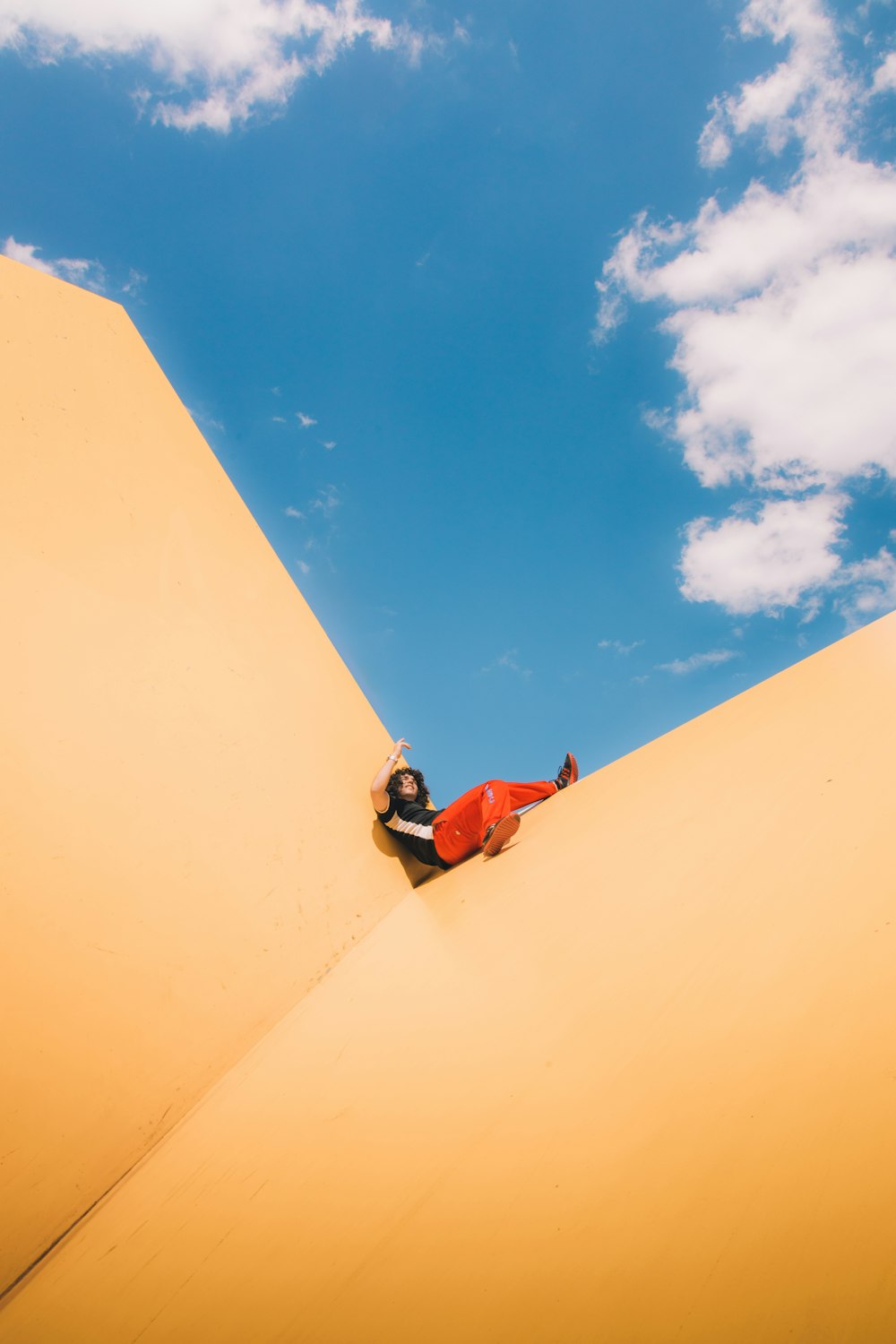 man in red shirt and blue denim jeans sitting on brown sand under blue sky during