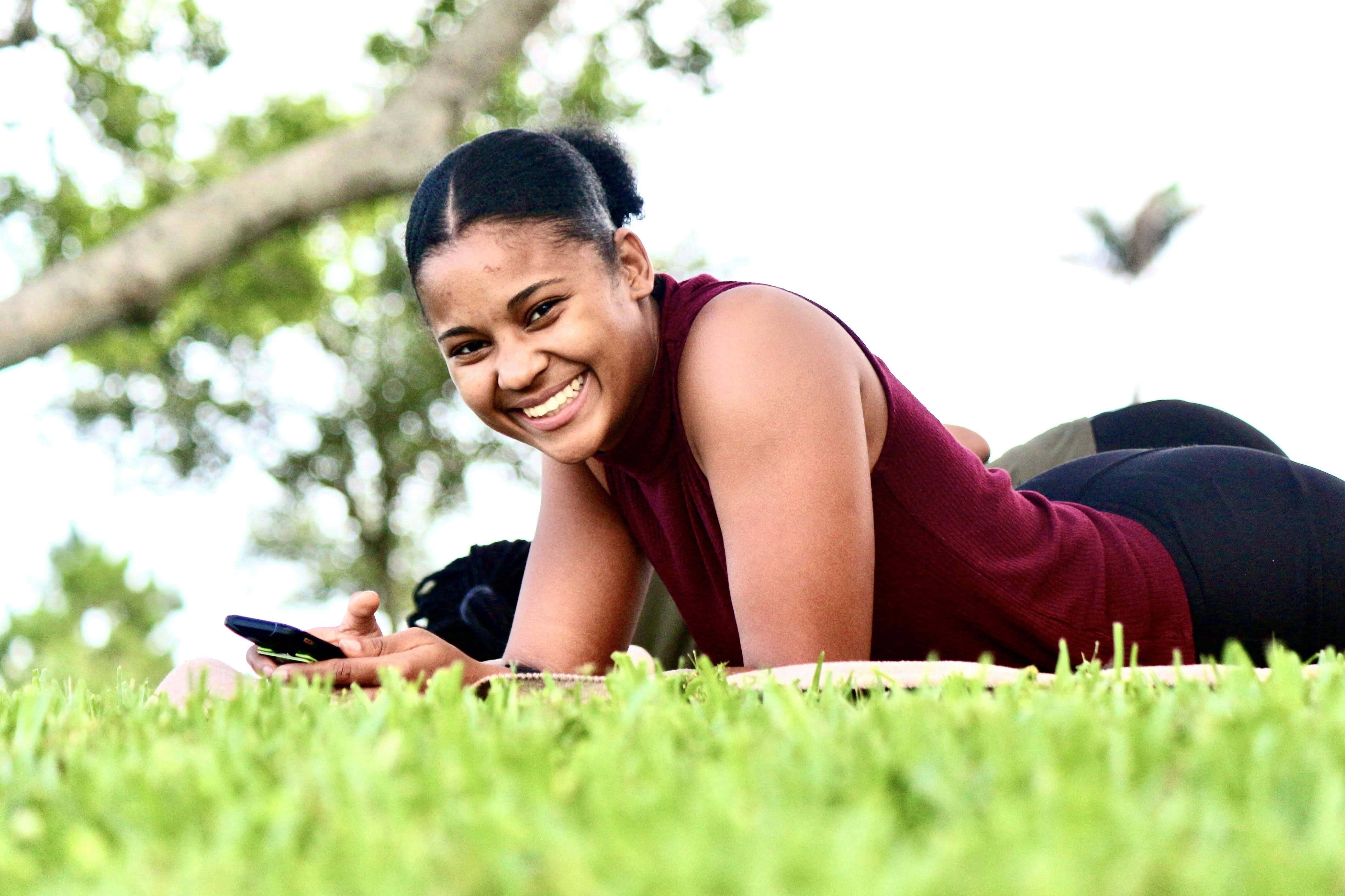 Wanita dengan tank top merah berbaring di rumput hijau di siang hari
