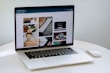 A laptop displaying a blog or webpage with images and text, sitting on a white table accompanied by a wireless mouse.