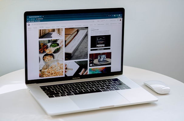 A laptop displaying a blog or webpage with images and text, sitting on a white table accompanied by a wireless mouse.