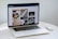 A laptop displaying a blog or webpage with images and text, sitting on a white table accompanied by a wireless mouse.