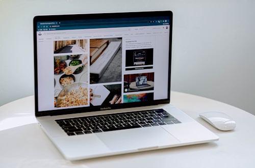 A laptop displaying a blog or webpage with images and text, sitting on a white table accompanied by a wireless mouse.