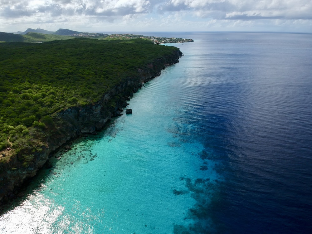 green grass covered mountain beside blue sea under white clouds during daytime