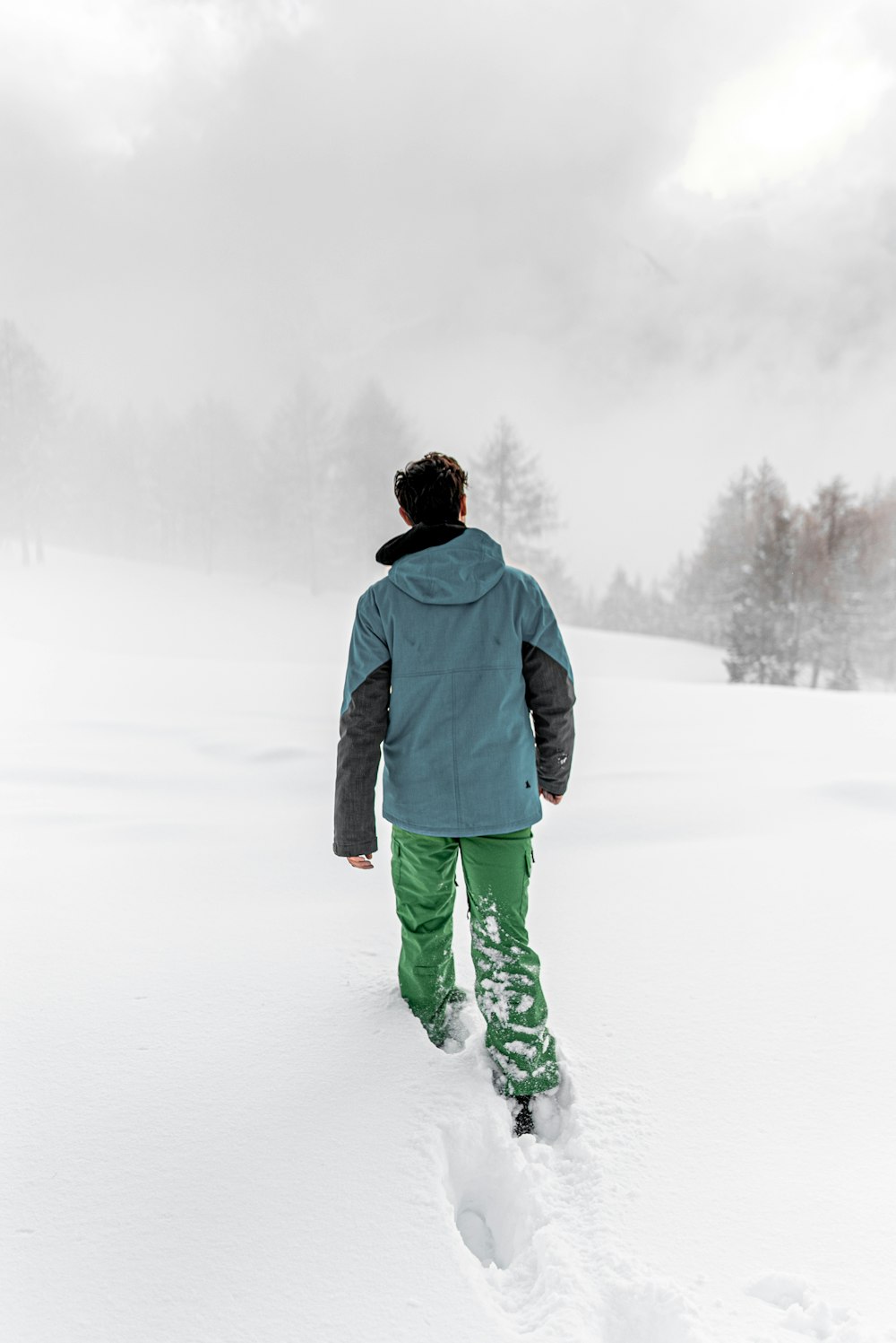 man in black hoodie and green pants standing on snow covered ground