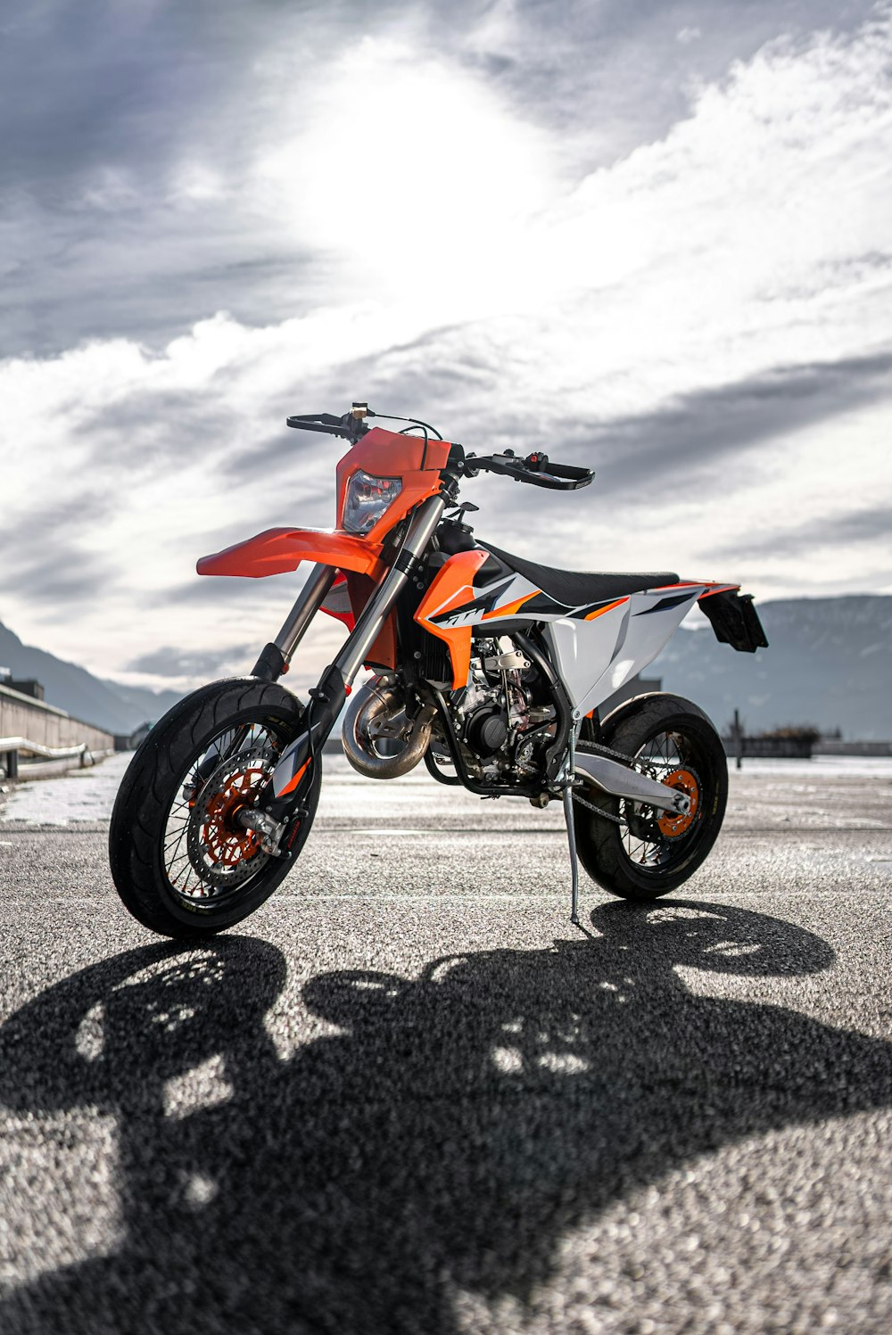 orange and black sports bike on gray sand under white clouds during daytime