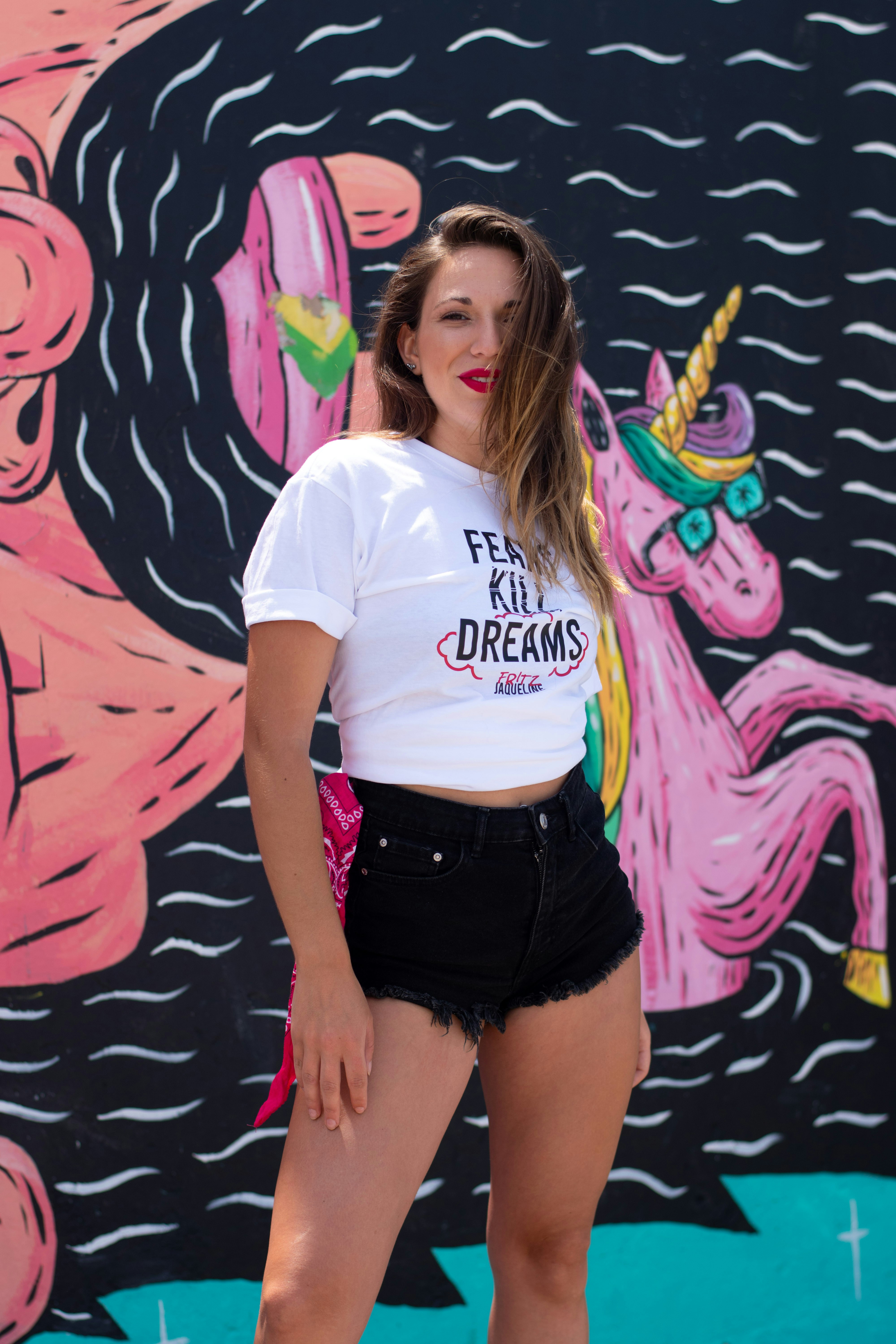 Frau in weißem T-Shirt und schwarzen Shorts an der Wand mit Graffiti