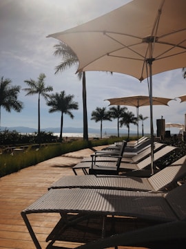 brown wooden outdoor table with chairs and umbrella near green trees during daytime
