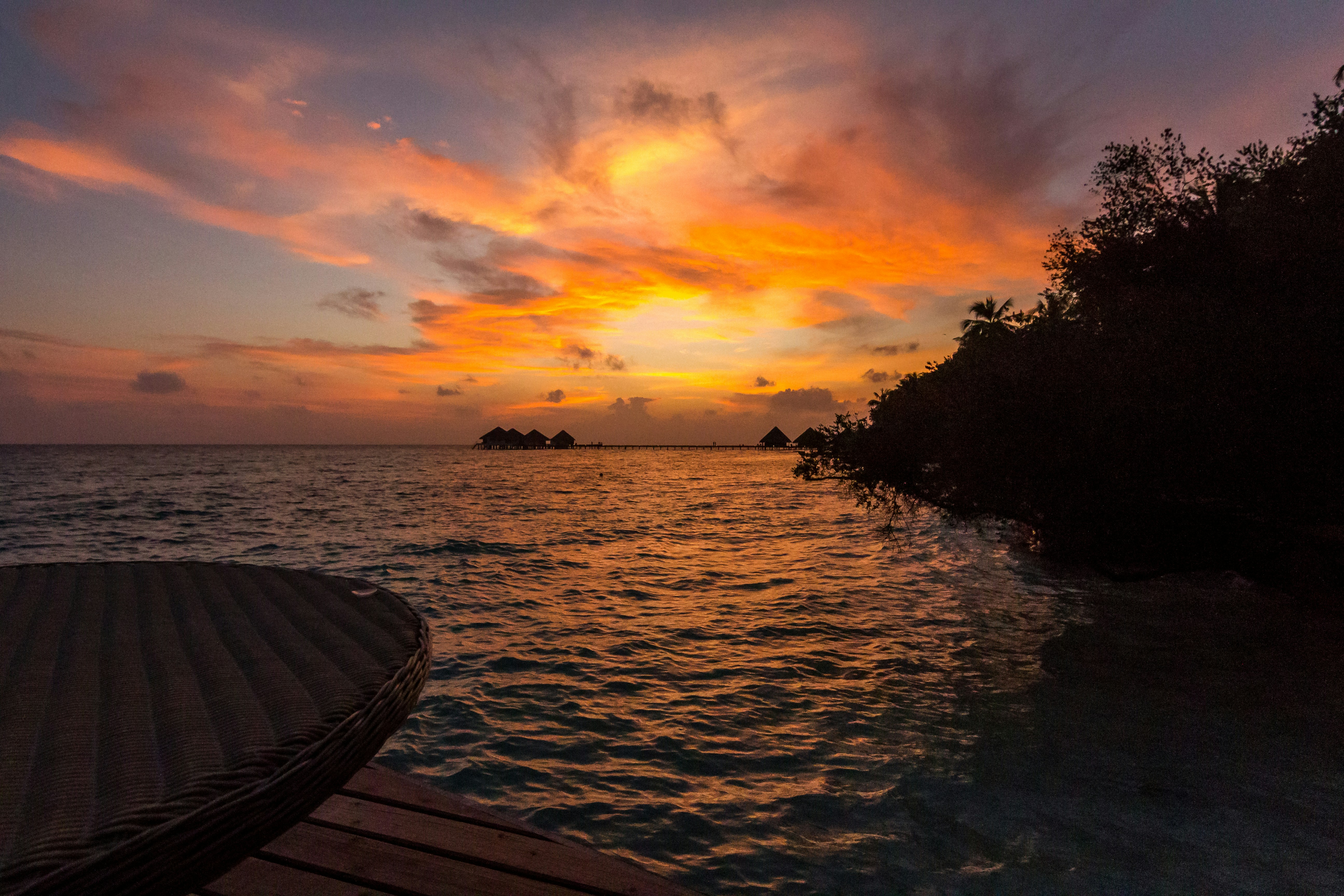 Bungalow sull acqua turchese delle Maldive con tramonto arancione sul mare
