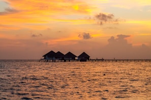 Overwater bungalows at sunset in the Maldives reflecting pink and orange hues.