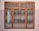 A window with a decorative metal grille featuring circular and arched patterns. The frame is painted brown, and the wall surrounding it is painted in two-tone colors, comprising a light beige and a darker shade.