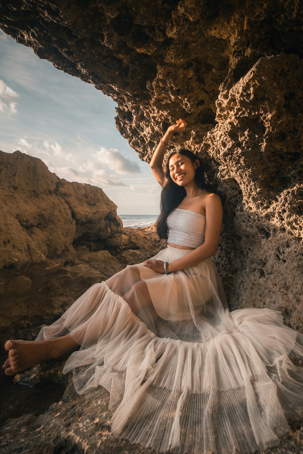 woman in white tube dress sitting on brown rock during daytime