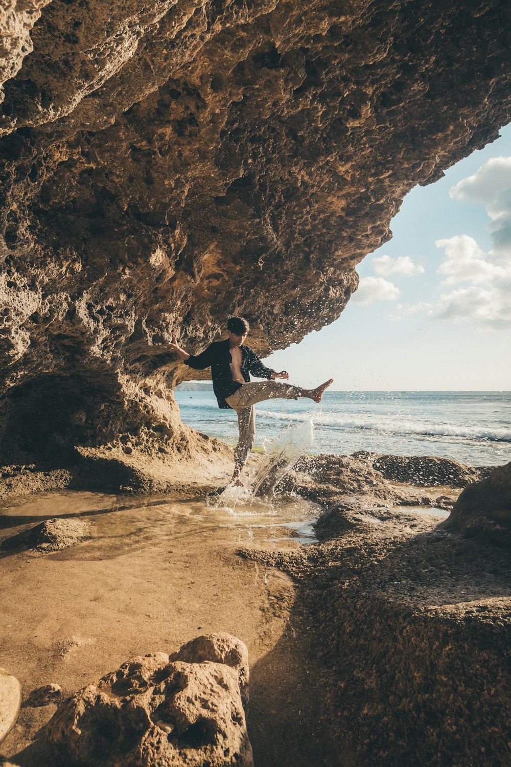 man in black shirt and black shorts jumping on brown rock formation during daytime