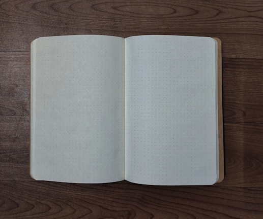 An open notebook with dot grid pages rests on a wooden surface, capturing a minimalist and organized setting.