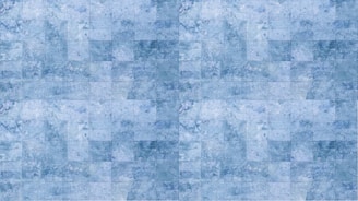 A pattern of blue square tiles arranged in a grid, each tile exhibiting variations in shading and texture, reminiscent of marble.