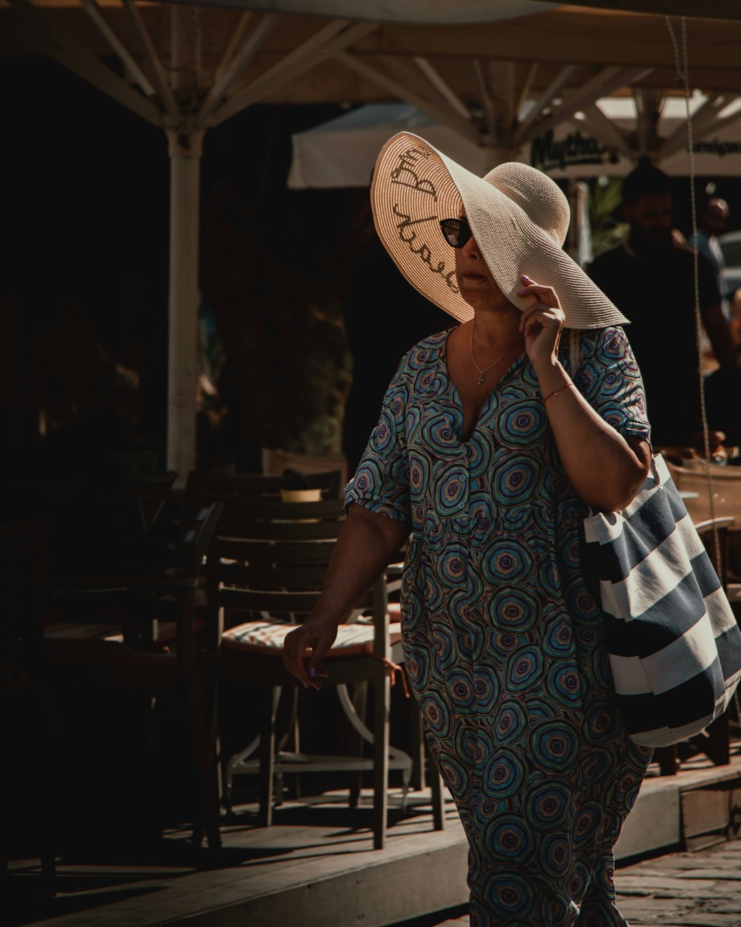 woman in blue and white floral dress wearing brown straw hat standing near brown wooden table
