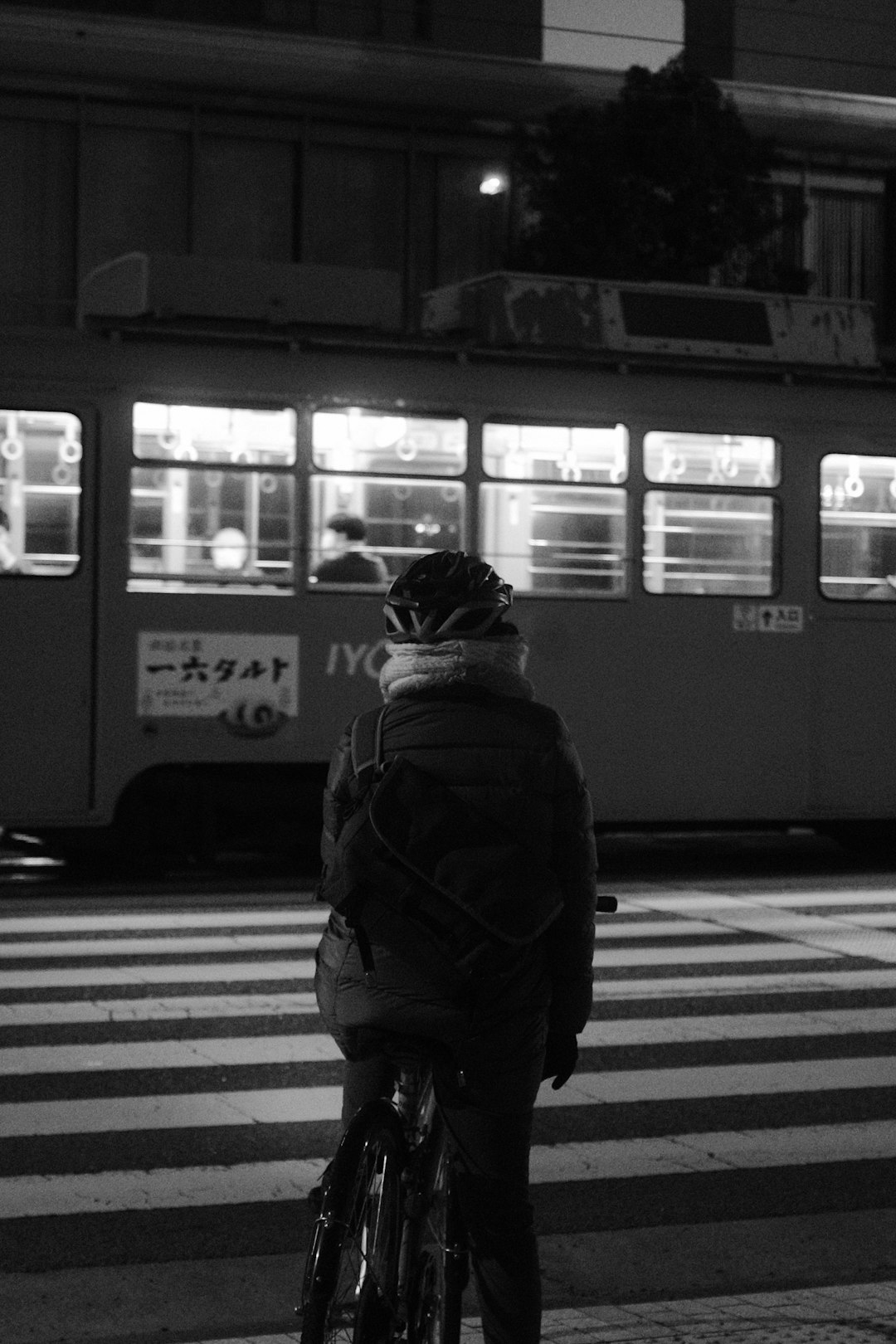 grayscale photo of person in black jacket and backpack standing in front of train