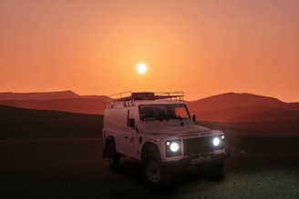 a white truck driving through a desert at sunset