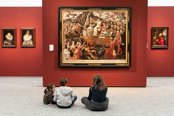 Three people—a young adult and two children—sitting on the floor of a gallery in front of a large artwork