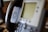A close-up view of an office IP phone with a blurred screen and keypad. The handset is resting on the phone cradle, and a speaker is visible on the side of the device.