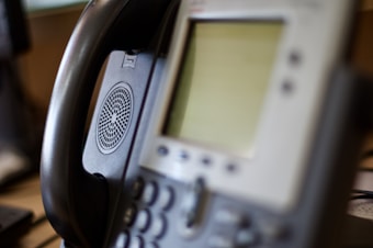 A close-up view of an office IP phone with a blurred screen and keypad. The handset is resting on the phone cradle, and a speaker is visible on the side of the device.