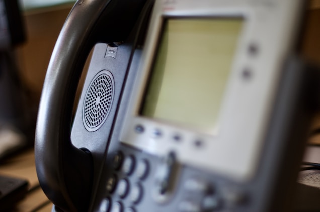 A close-up view of an office IP phone with a blurred screen and keypad. The handset is resting on the phone cradle, and a speaker is visible on the side of the device.