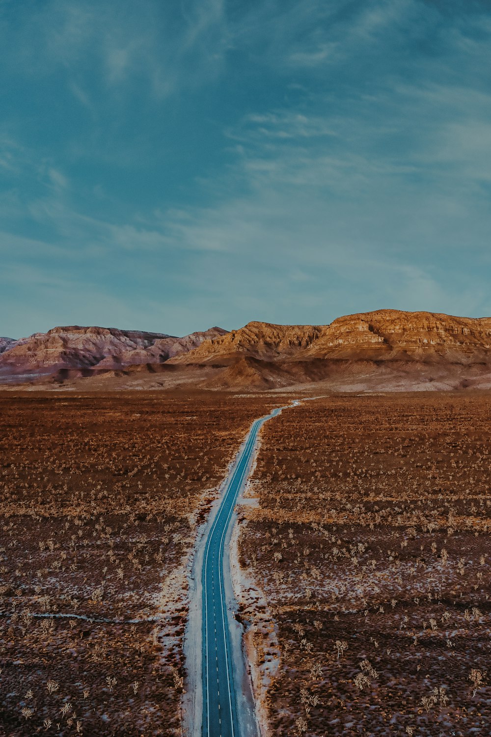 Carretera de asfalto gris entre montañas marrones bajo cielo azul durante el día